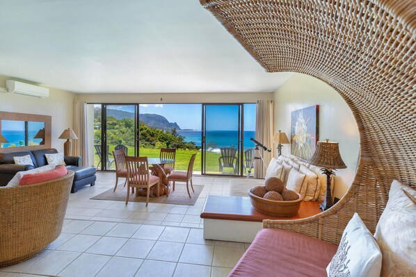 A spacious living area with a large sliding glass door leading to a balcony overlooking a scenic ocean view. - Puu Poa 112, 2bd/2ba sleeps 5 A/C oceanfront, pool tennis Best Bali Hai view (Princeville)