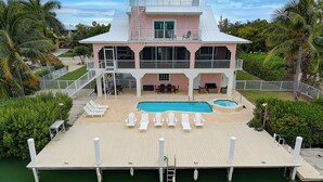 Una casa de dos pisos con piscina, sillas de terraza y bañera de hidromasaje.