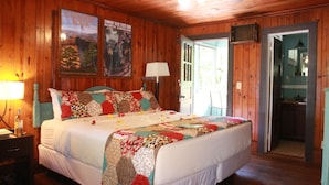 A wooden-paneled bedroom with a large bed, a nightstand, a lamp, and a poster of Chimney Rock State Park. - The Riverside Lodge at Chimney Rock (Chimney Rock)