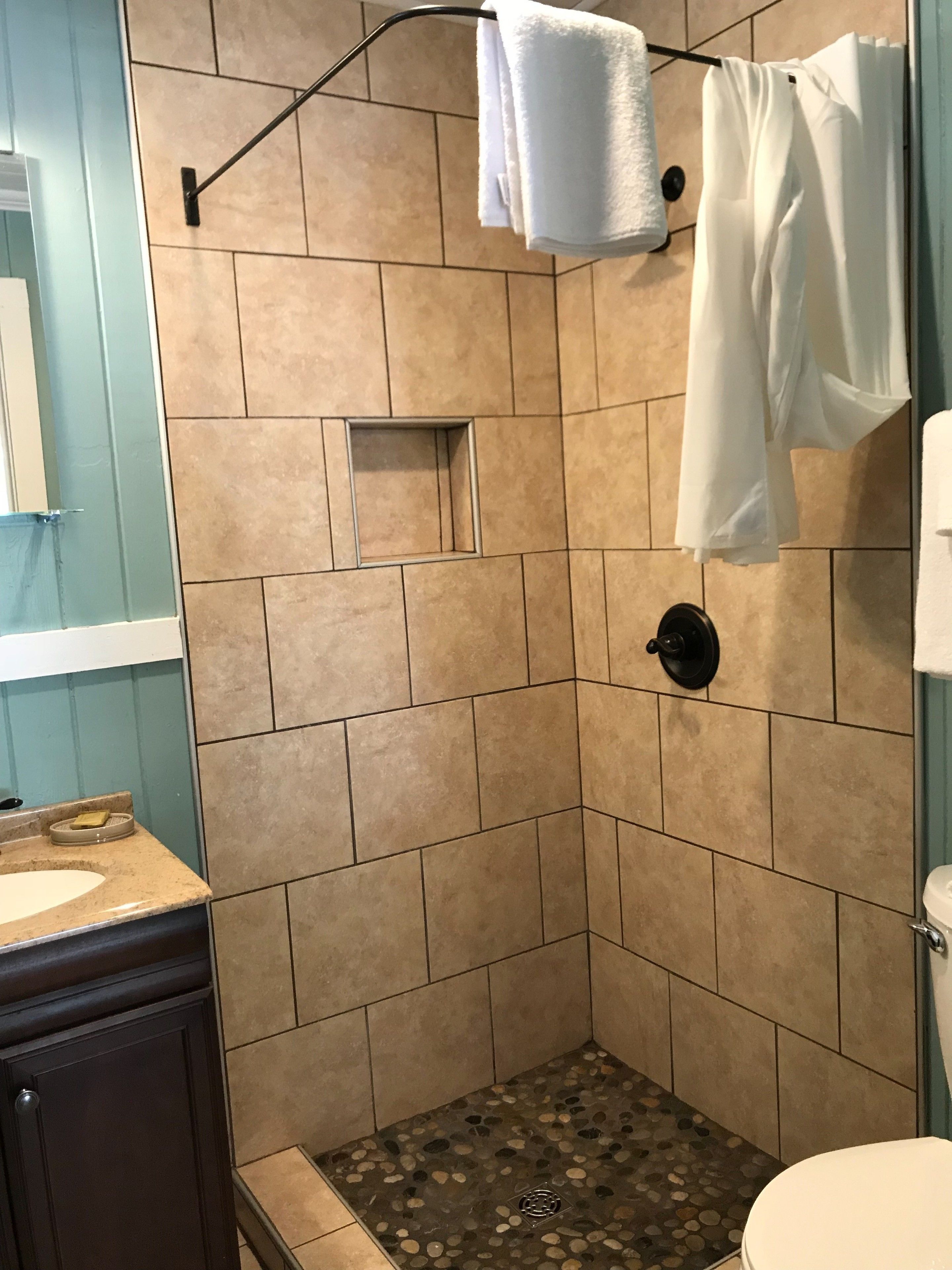 A shower with beige tiles, a glass door, and a small shelf.
