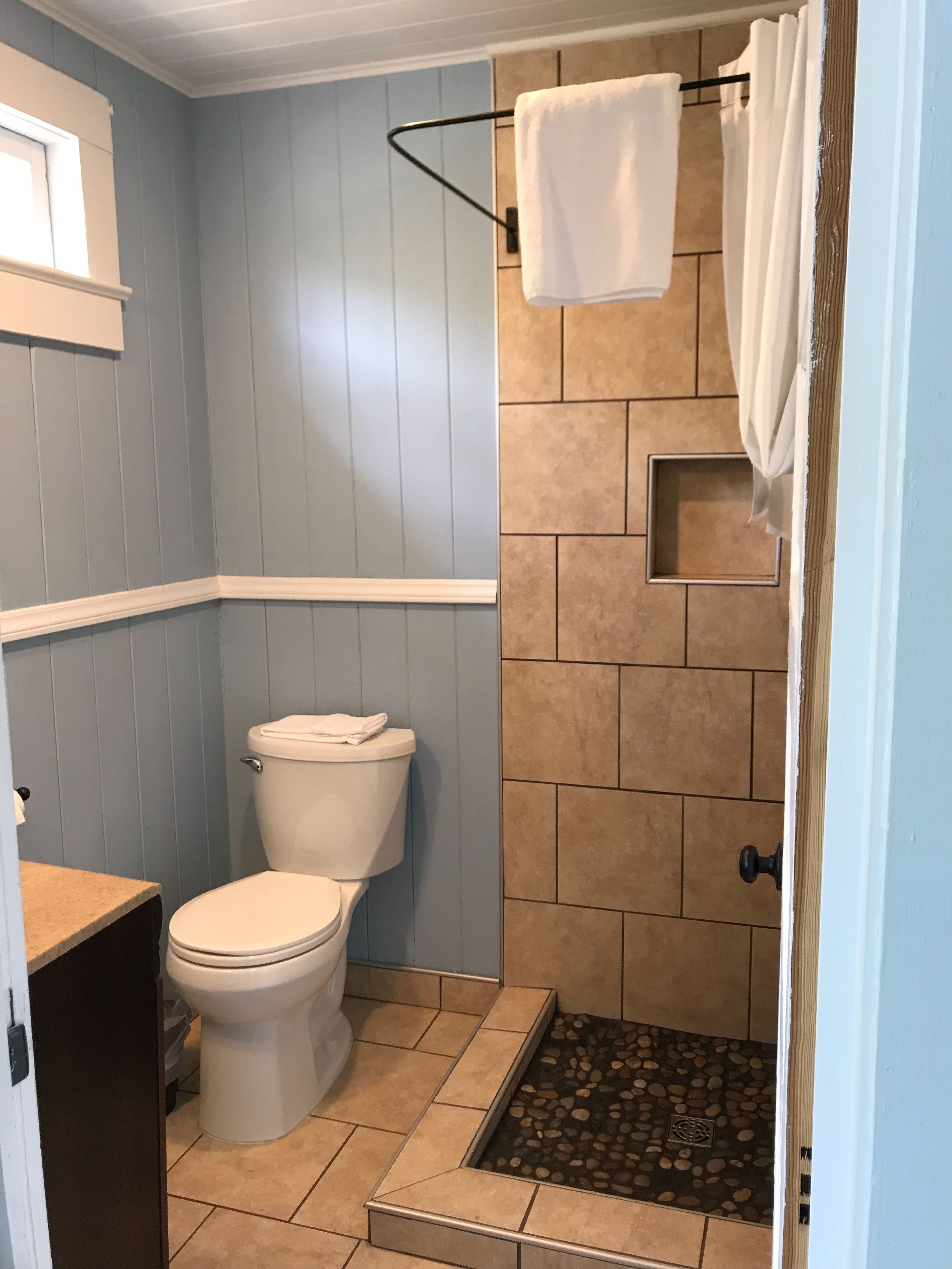 A bathroom with a toilet, shower, and a small window.