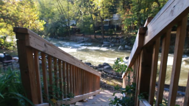 A wooden bridge over a river with a rocky riverbank and greenery in the background. - The Riverside Lodge at Chimney Rock (Chimney Rock)