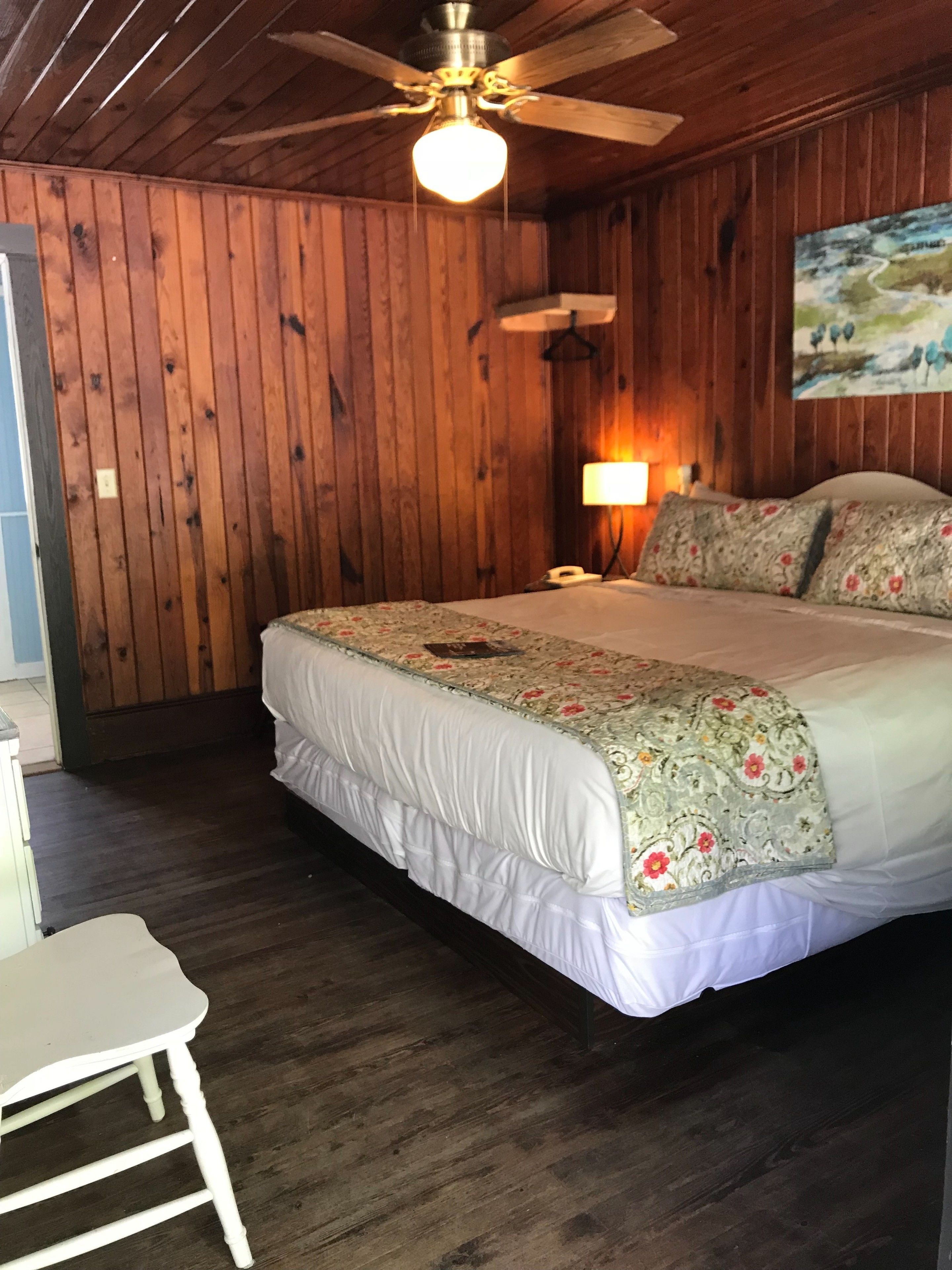 Una habitación con paneles de madera, una cama, un escritorio y un ventilador de techo.