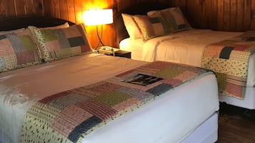 A room with two beds, wooden walls, a ceiling fan, and a wall-mounted lamp.