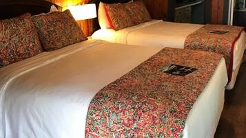 Ein Zimmer mit Holzwänden und einem Deckenventilator. Es gibt zwei Betten mit blumigem Überwurf und einen kleinen Schreibtisch mit Stuhl.