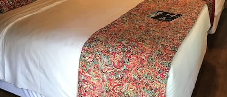 A room with wooden walls and a ceiling fan. There are two beds with floral bedspreads and a small desk with a chair.