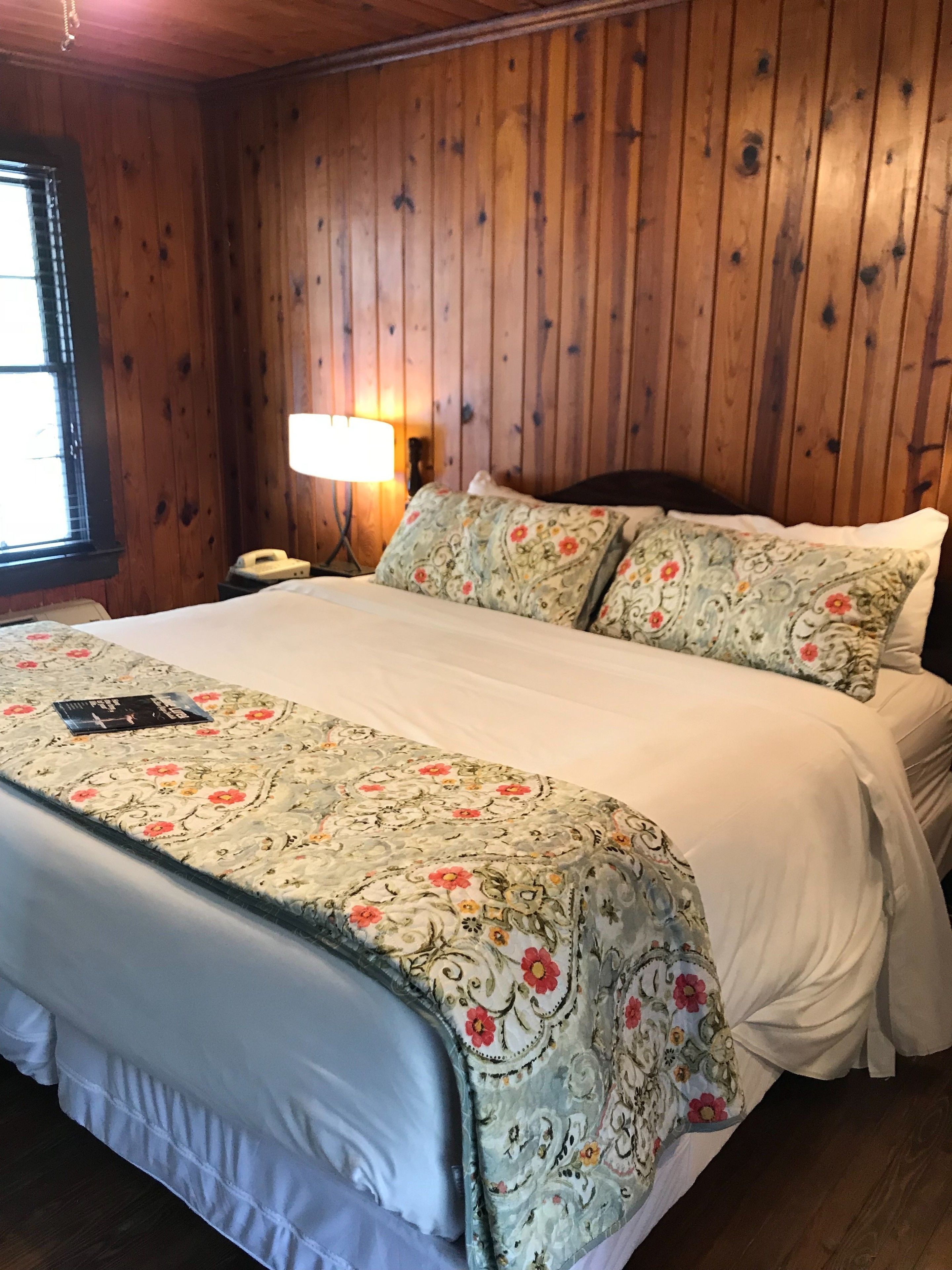 Quarto com painéis de madeira, uma cama, abajur e janela.
