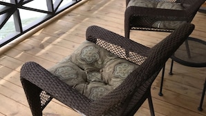 A wooden deck with two wicker chairs and a metal table. - The Riverside Lodge at Chimney Rock (Chimney Rock)