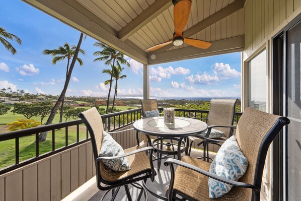 A covered outdoor seating area with a table and chairs, overlooking a scenic view of palm trees and a distant landscape.