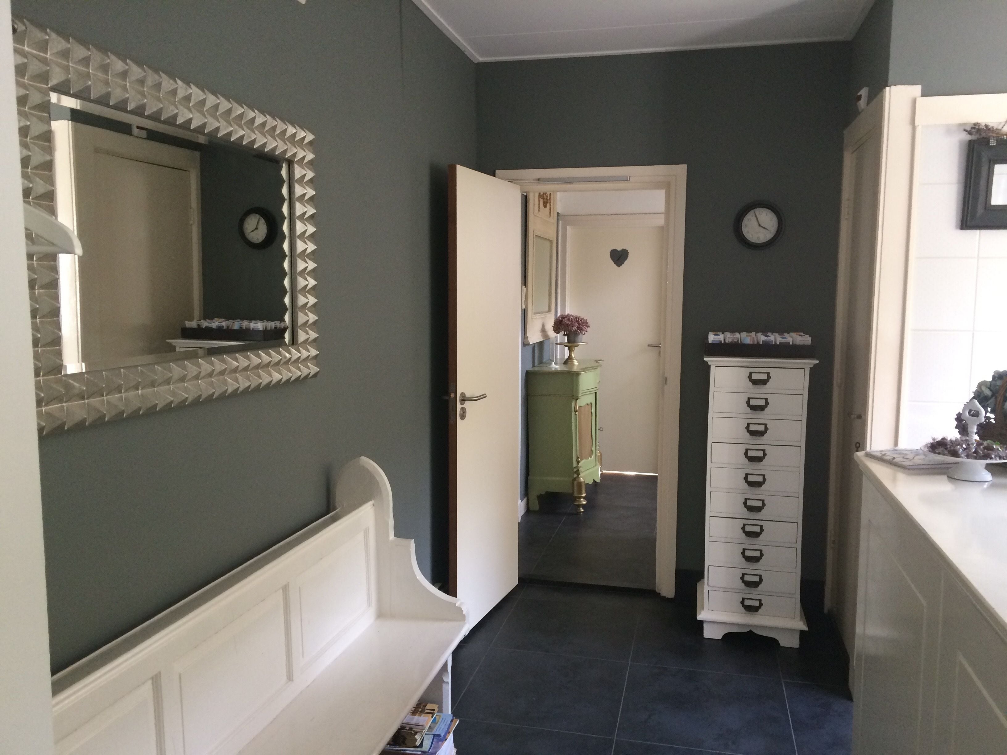 Un pasillo con un aparador blanco, un mueble verde y un espejo en la pared izquierda.