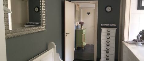 Un pasillo con un aparador blanco, un mueble verde y un espejo en la pared izquierda.