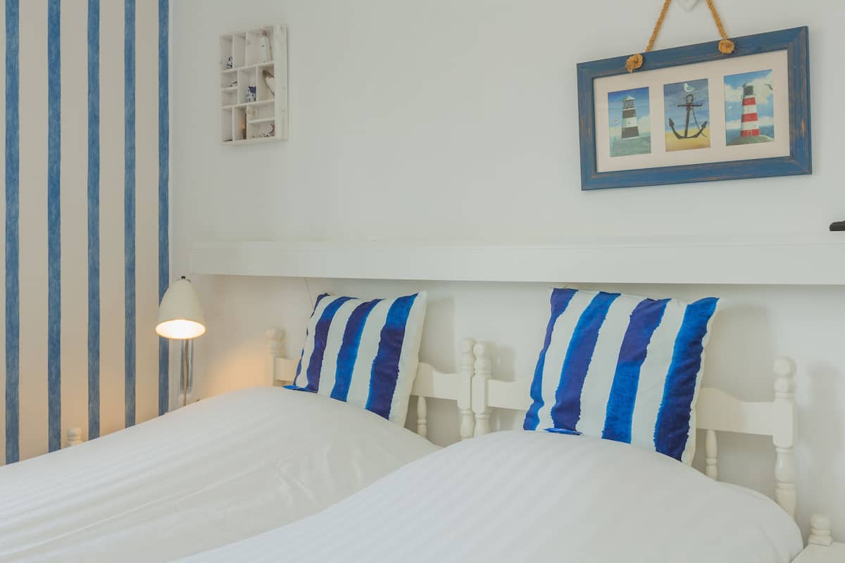 A bedroom with two beds, striped pillows, a bedside lamp, and a framed picture on the wall.