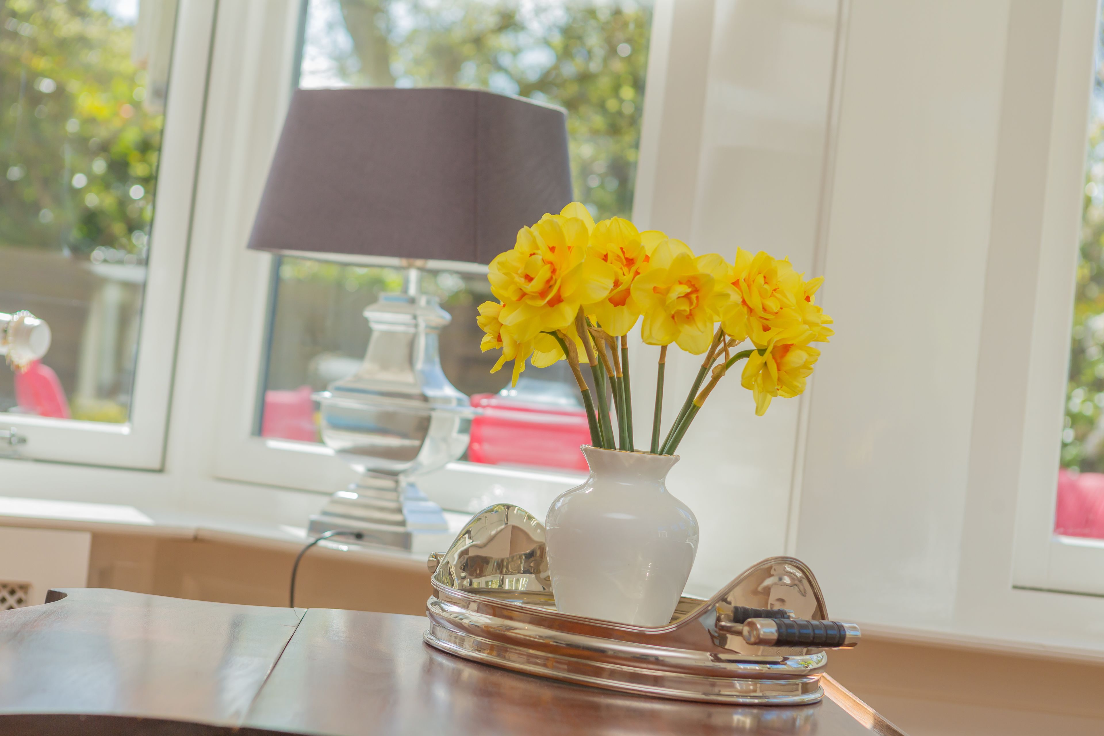 Een tafel met een witte vaas gevuld met gele bloemen, een lamp en een dienblad met een pen en decoratie.