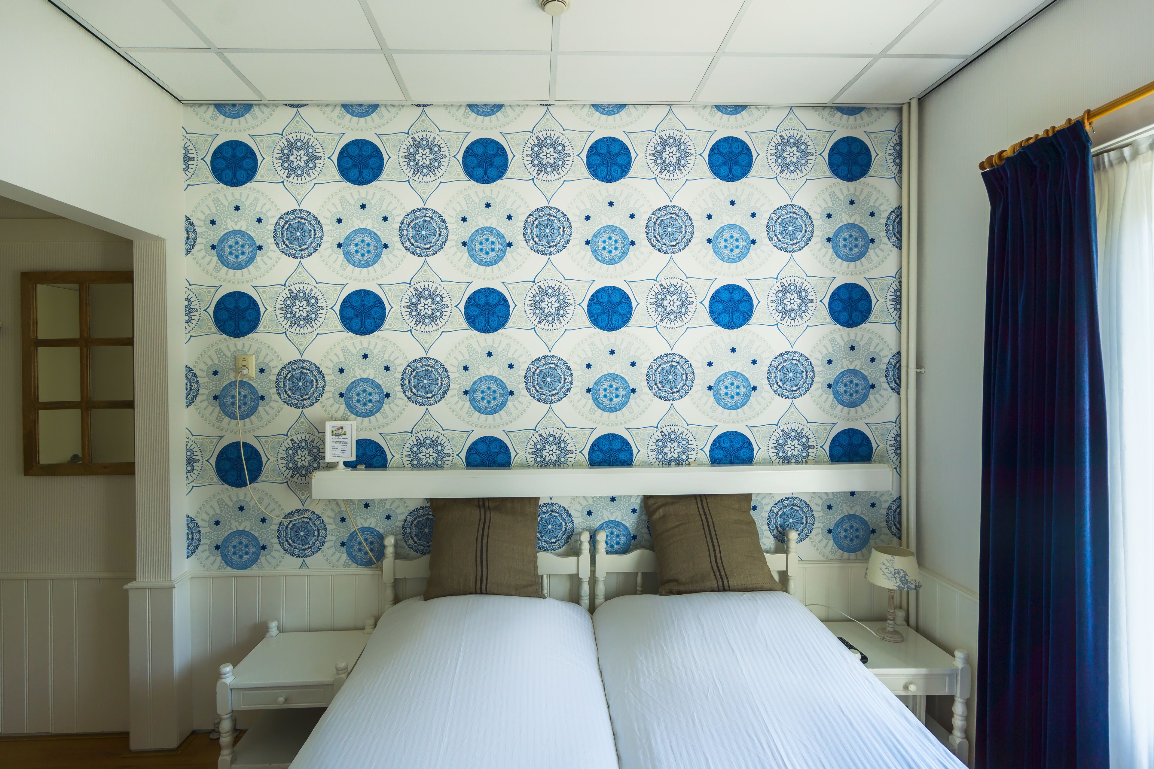 A room with a bed, a bedside table, and a wall with a blue and white patterned design.