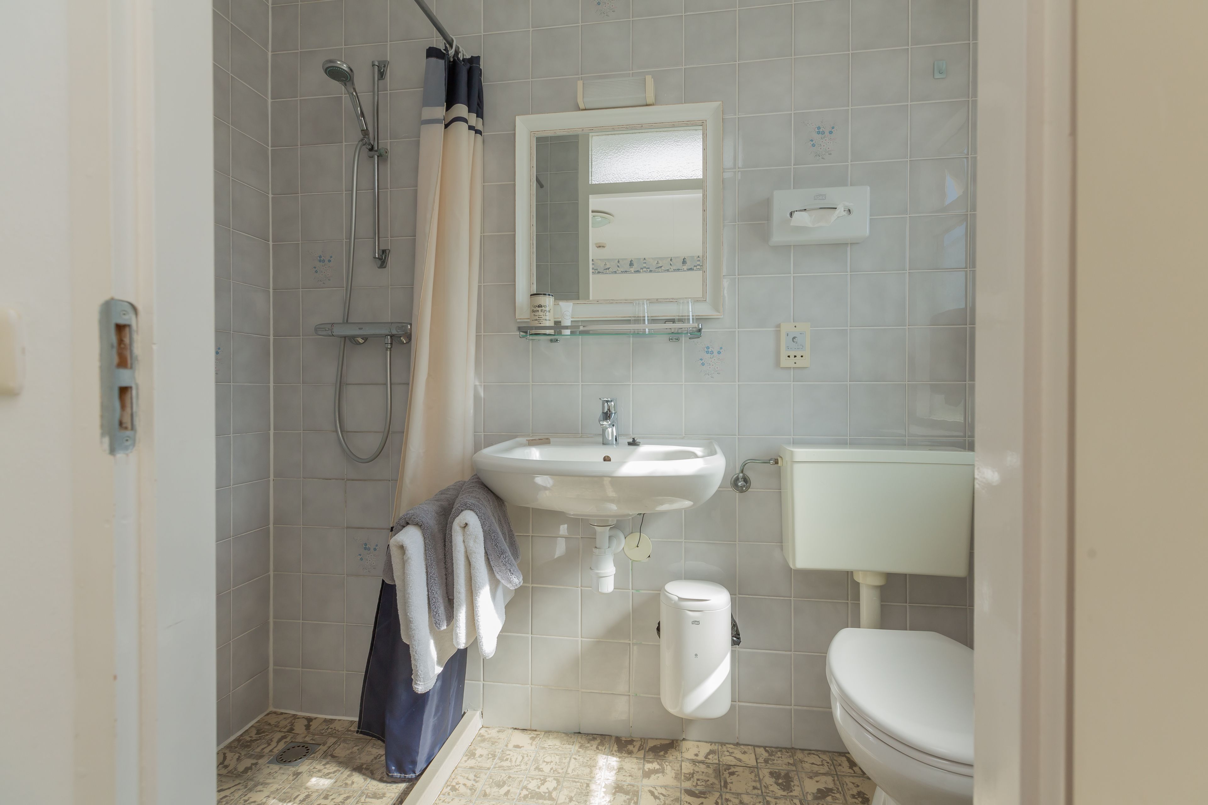 A bathroom with a shower, sink, toilet, and a glass shelf above the sink.
