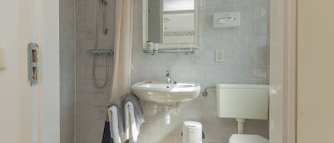A bathroom with a shower, sink, toilet, and a glass shelf above the sink.