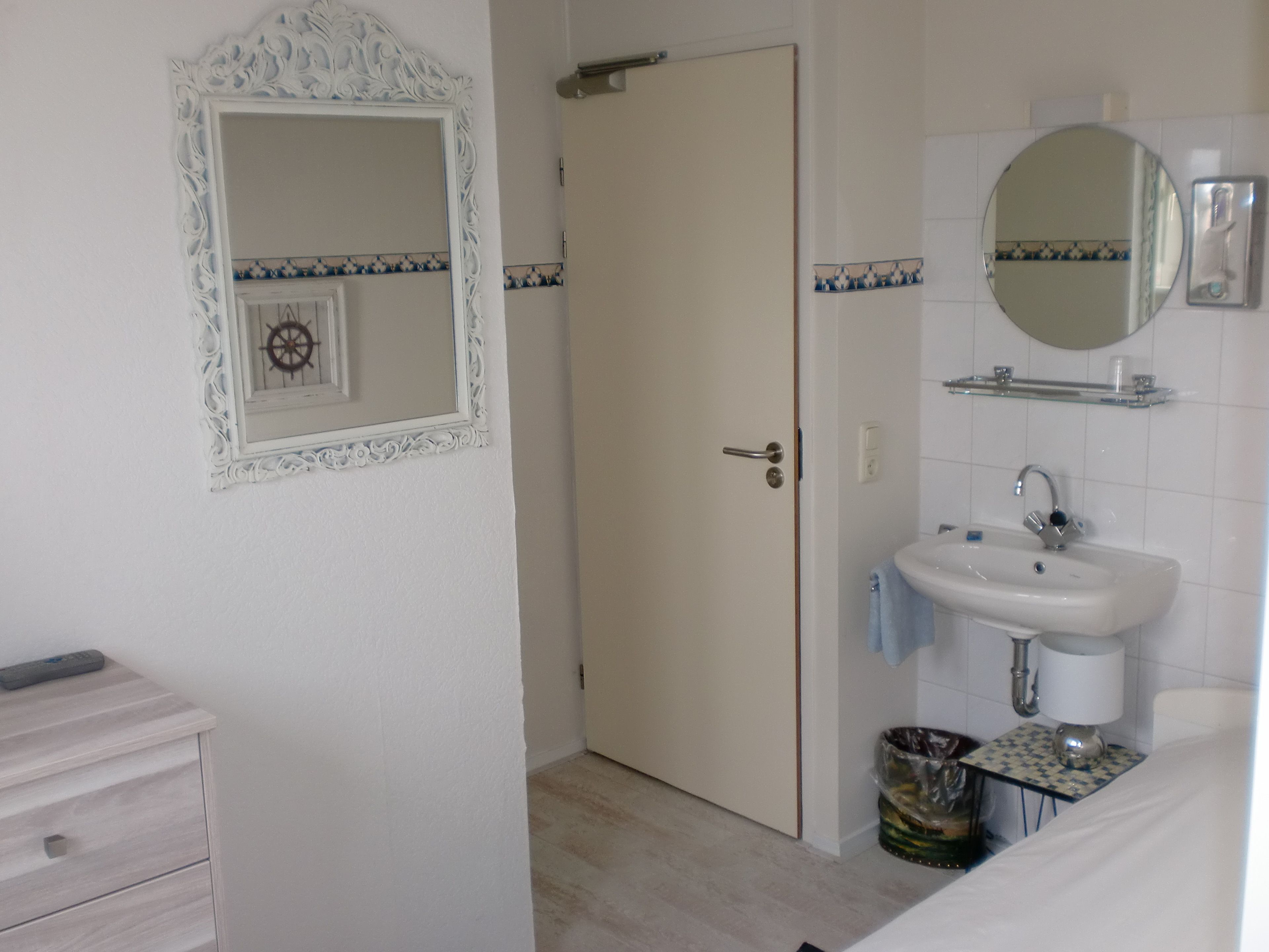 A bathroom with a white door, a sink with a mirror above it, and a small trash bin.