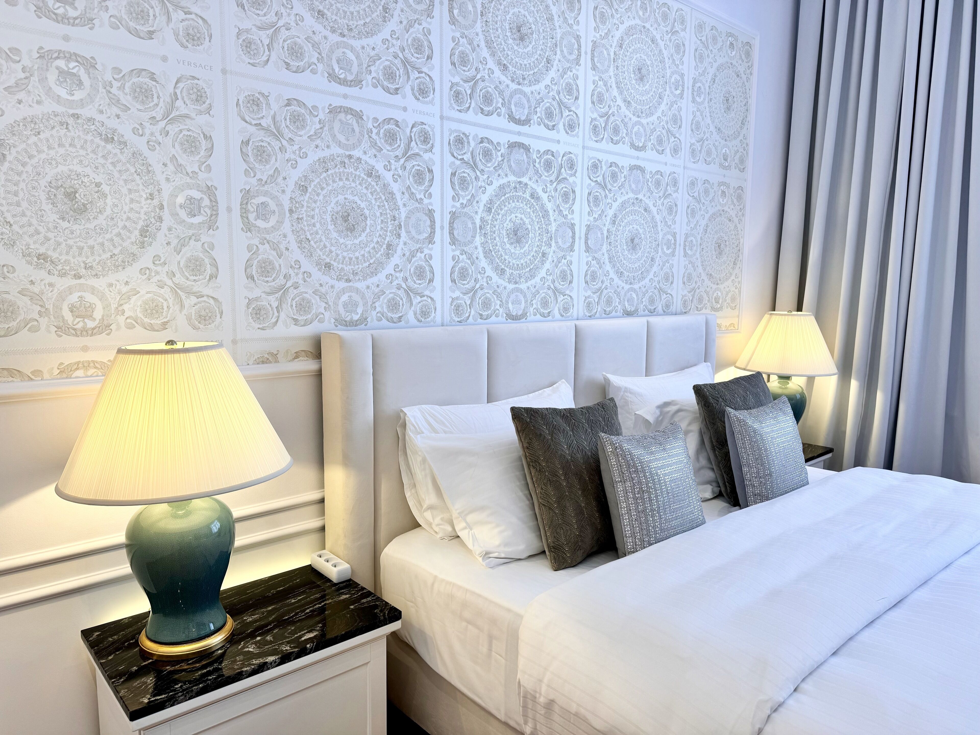 A neatly made bed with white linens and decorative pillows, flanked by two bedside lamps on a marble nightstand.