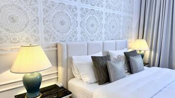 A neatly made bed with white linens and decorative pillows, flanked by two bedside lamps on a marble nightstand.