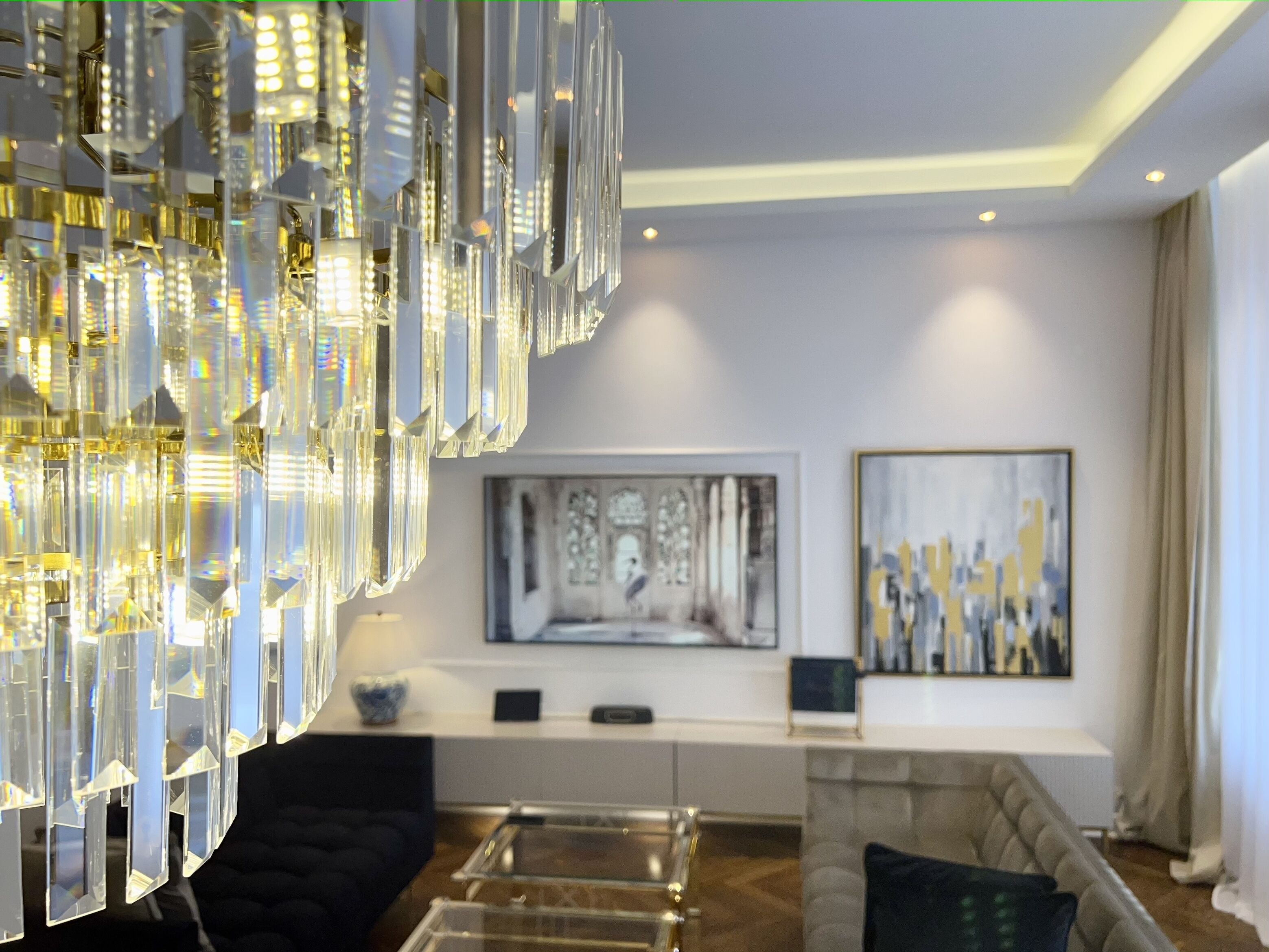 A modern living room with a large chandelier, a sofa, a coffee table, and artwork on the walls.