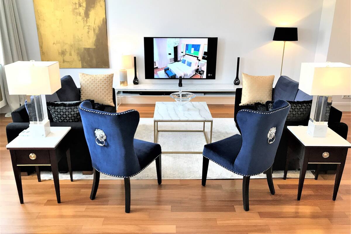 Un salon moderne doté d’un téléviseur à écran plat, de deux fauteuils bleus, d’une table basse et de deux petites tables d’appoint avec des lampes.
