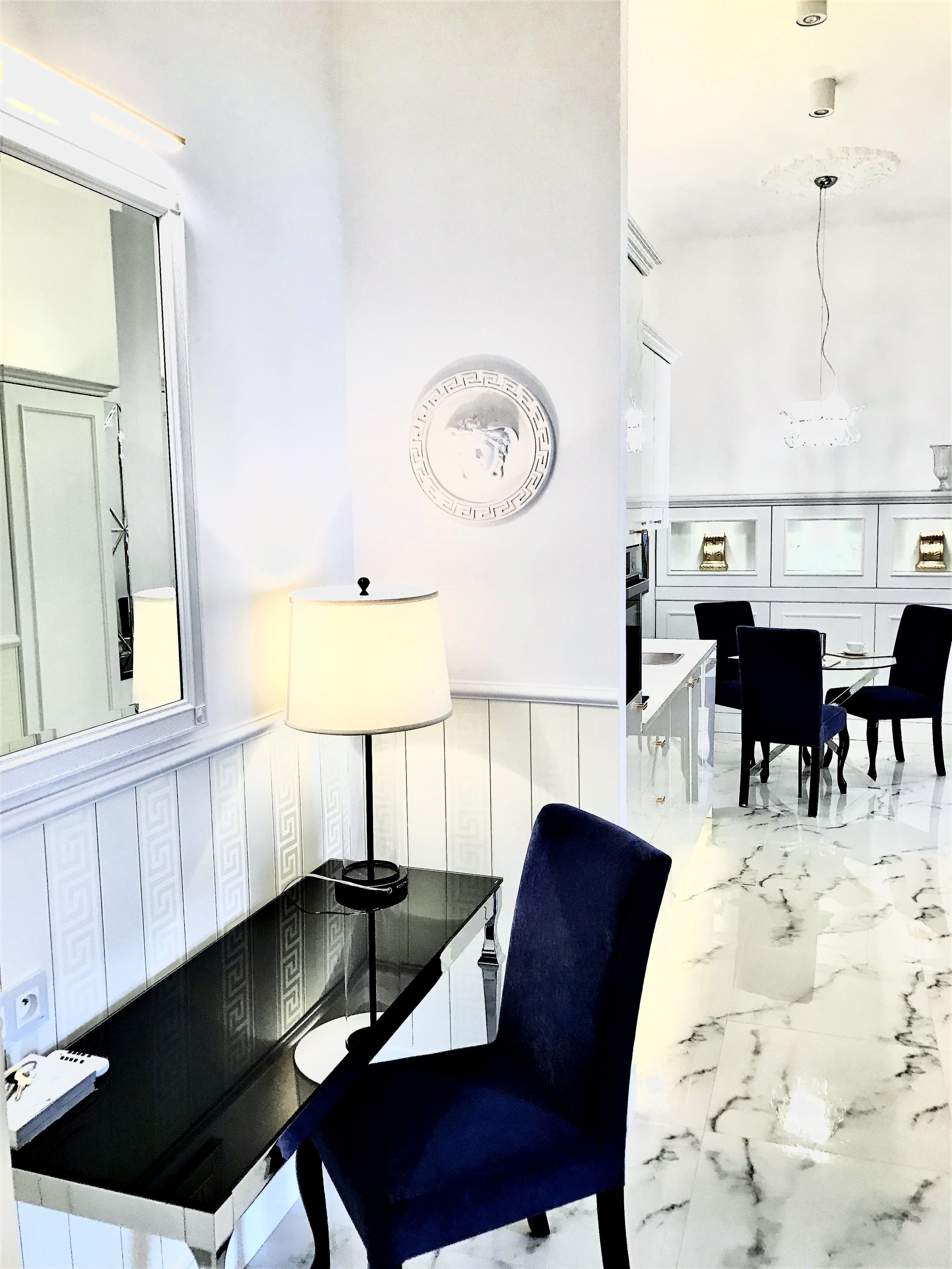 Ein Zimmer mit Schreibtisch, Stuhl, Lampe und einem Essbereich mit Stühlen und Tisch.