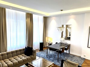 Een moderne hotelkamer met een bank, een eettafel, stoelen en een groot raam met gordijnen.