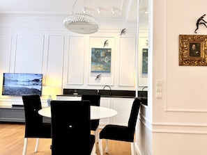 Ein moderner Essbereich mit einem weißen Tisch, schwarzen Stühlen, einer Kristallleuchter und Kunstwerken an den Wänden.