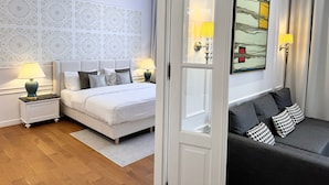 Une chambre d’hôtel avec un lit blanc, deux lampes de chevet, un papier peint à motifs et une œuvre d’art encadrée accrochée au mur.