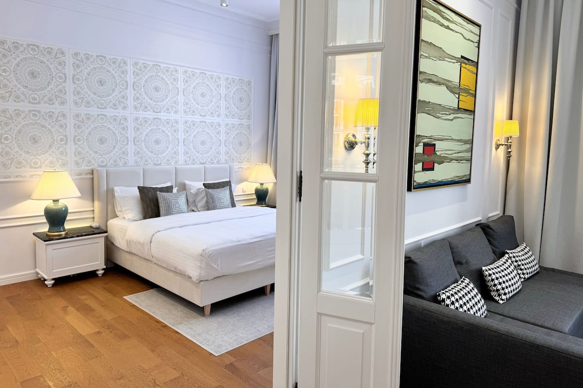 Une chambre d’hôtel avec un lit blanc, deux lampes de chevet, un papier peint à motifs et une œuvre d’art encadrée accrochée au mur.