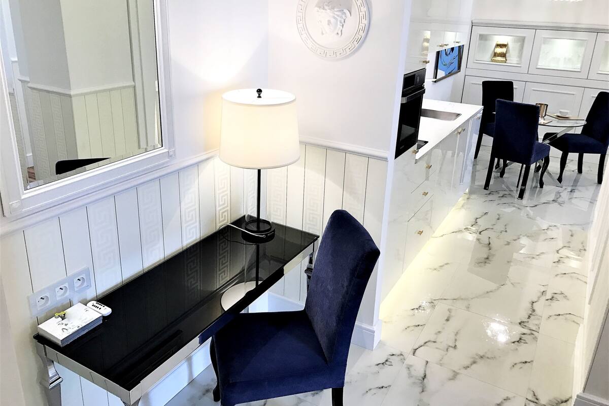 Une chambre d’hôtel moderne avec un bureau noir, une chaise bleue, une table ronde avec des chaises, un téléviseur et un élément décoratif mural.