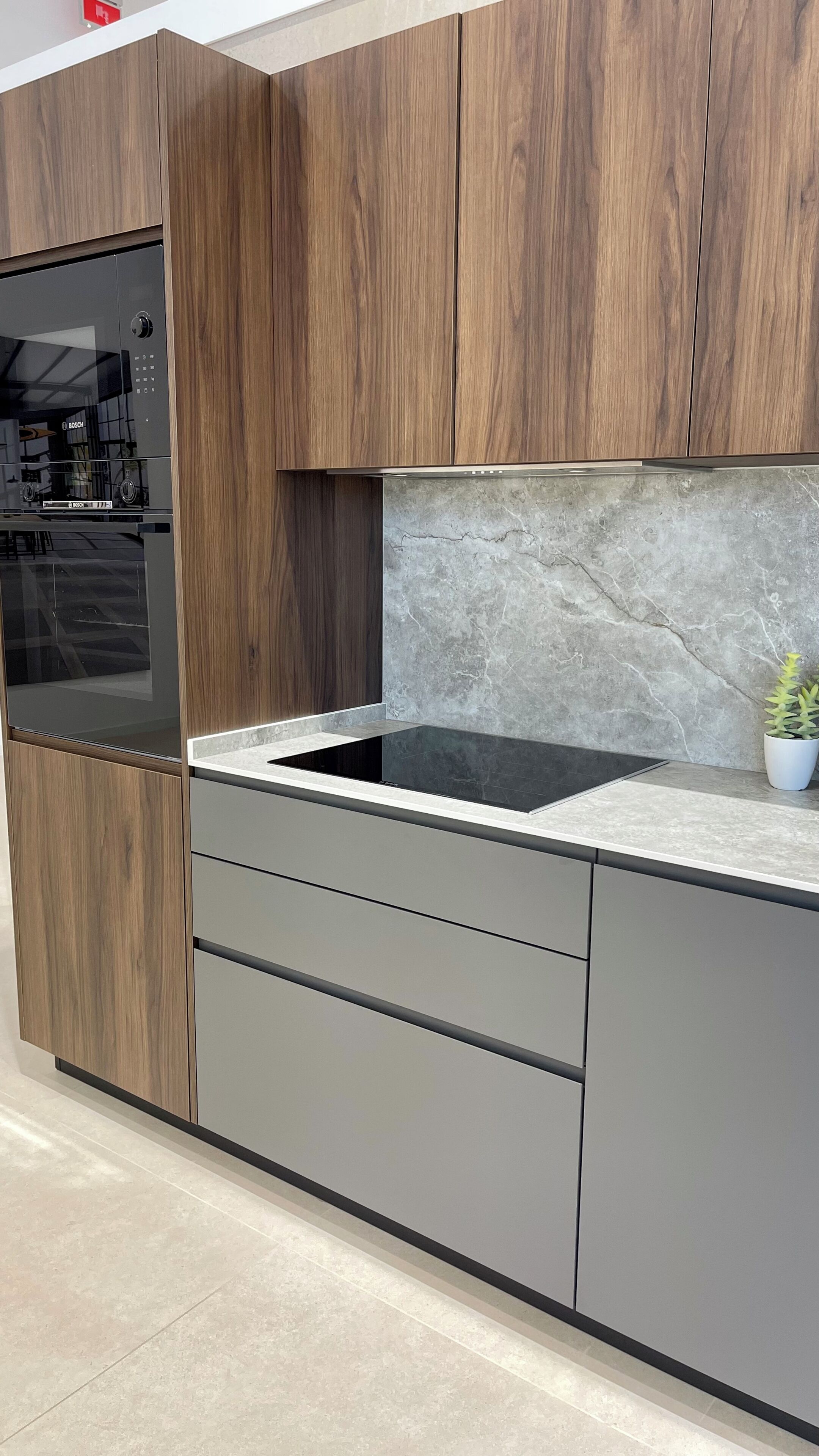 Eine moderne Küche mit Holzausstattung, integriertem Backofen, Marmorfliesenspiegel und einem kleinen Topfpflanzen.