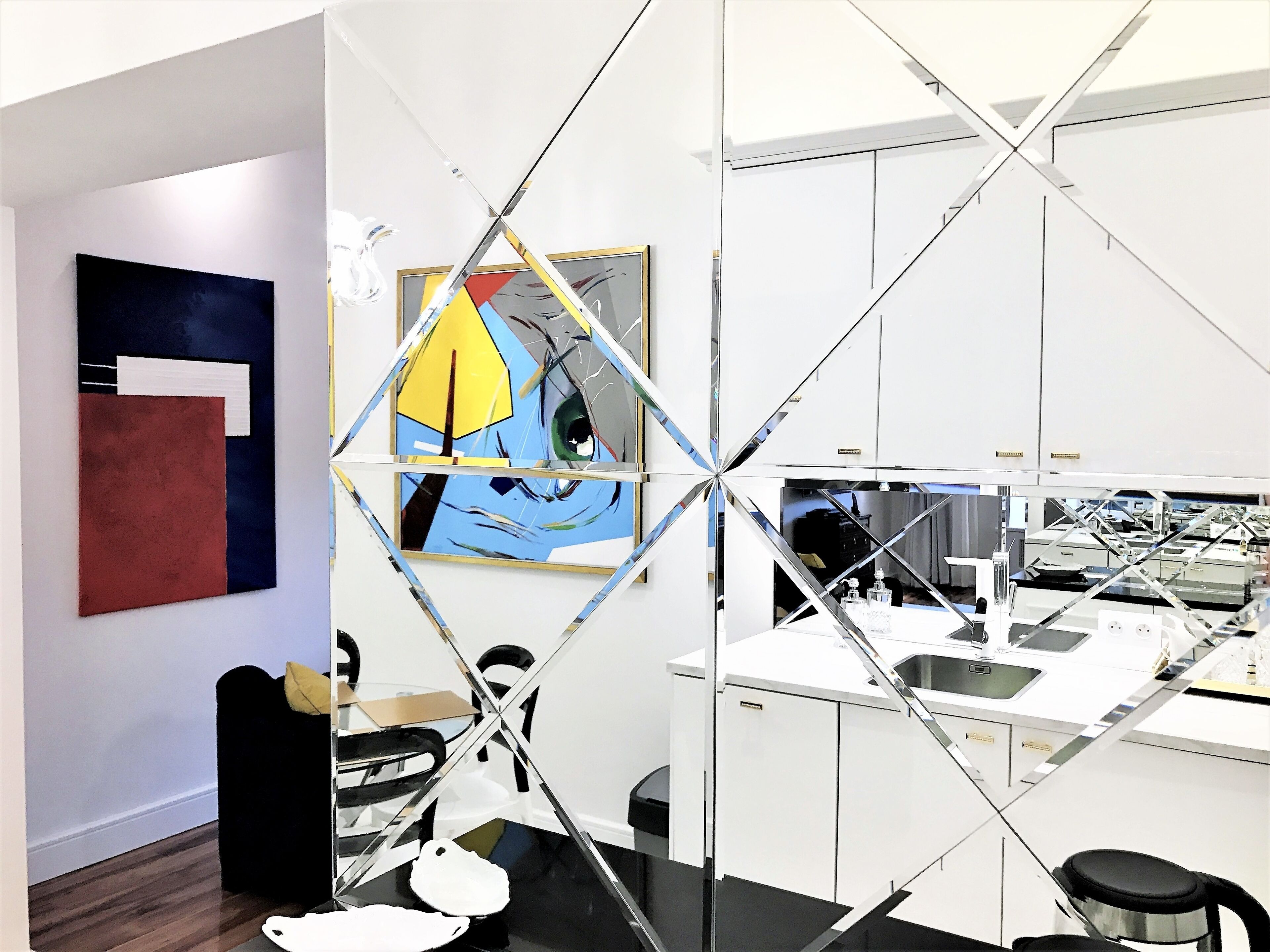 A modern office space with a glass partition, a painting on the wall, and a desk area with a computer and office supplies.