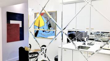 A modern office space with a glass partition, a painting on the wall, and a desk area with a computer and office supplies.