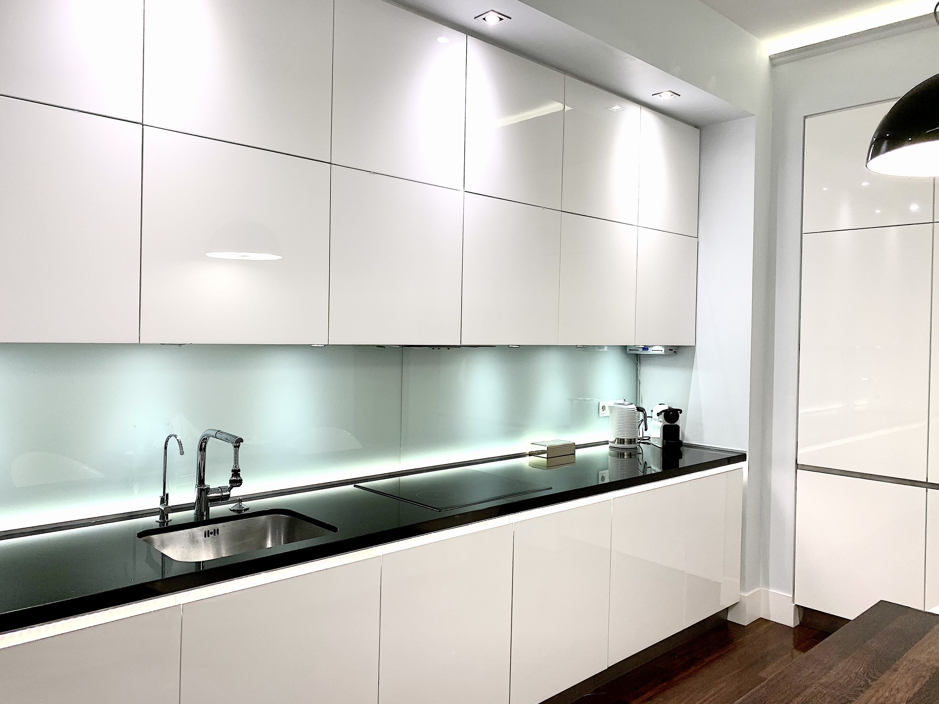 A modern kitchen with white cabinets, a black countertop, and a stainless steel sink.