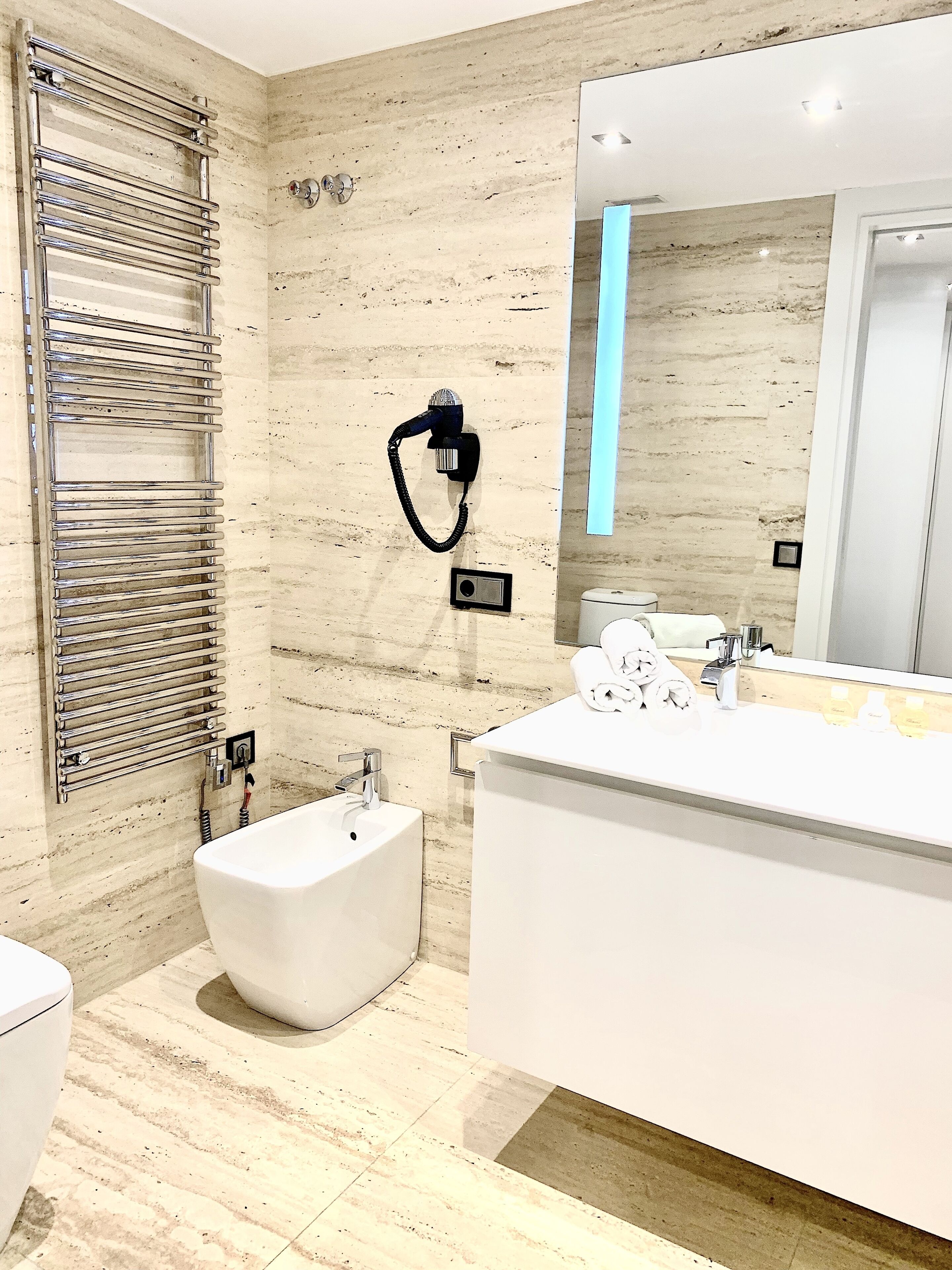 A modern bathroom with a bidet, a large mirror, and a towel rack.