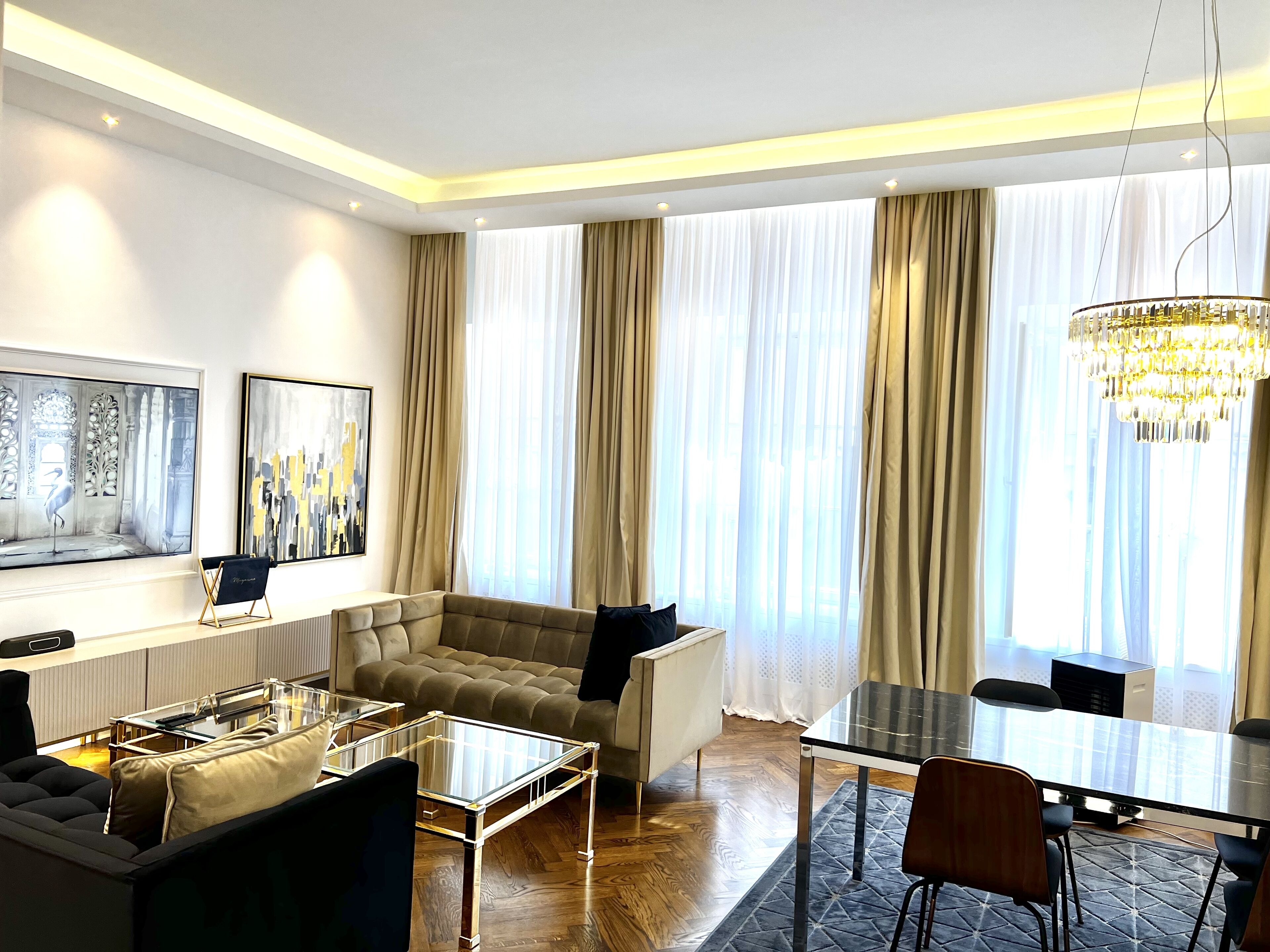 A modern living room with a sectional sofa, a glass coffee table, a dining table with chairs, and a chandelier.