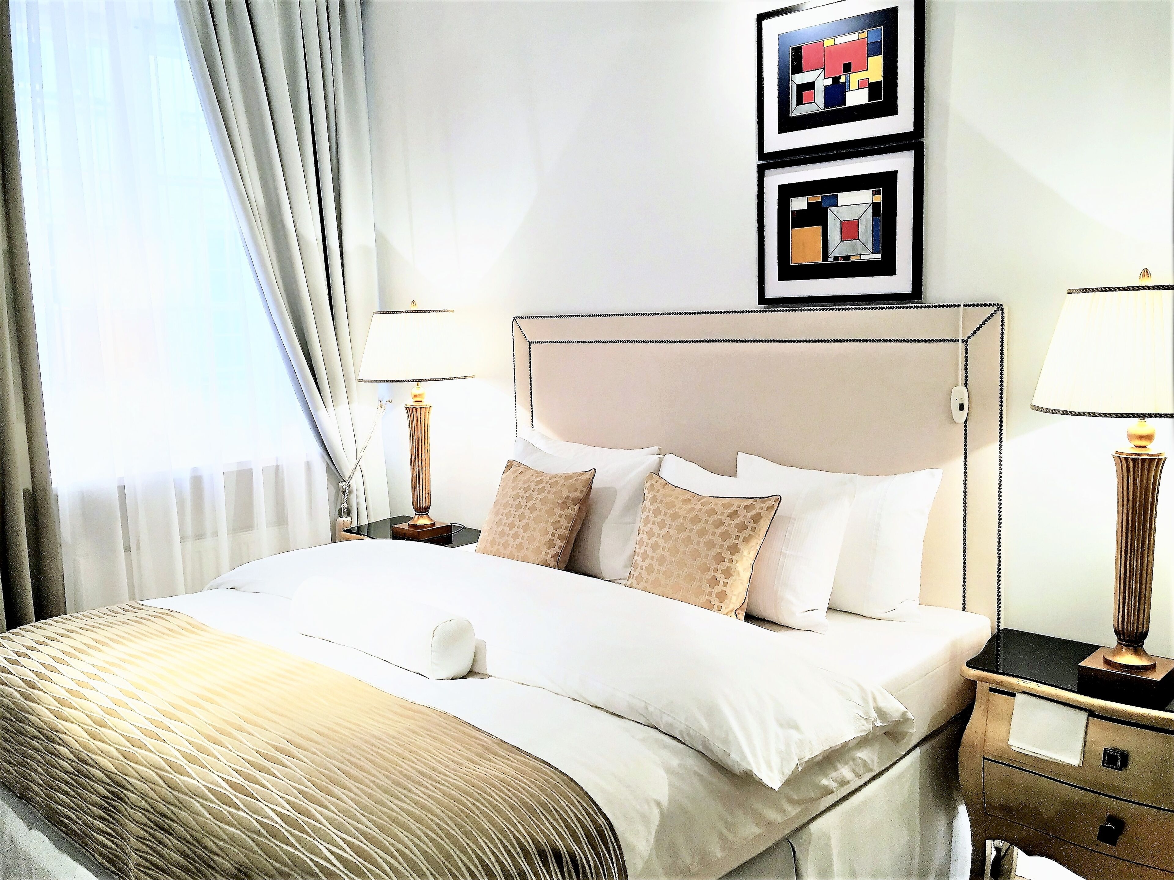 A neatly made bed with a headboard, two bedside tables with lamps, and a framed picture on the wall.