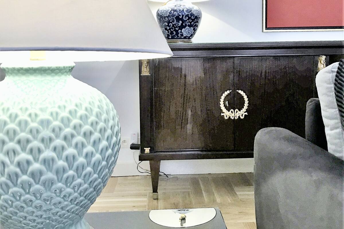 Un salon avec un grand vase bleu, une lampe de table, un meuble orné d’une guirlande décorative et un tableau encadré accroché au mur.