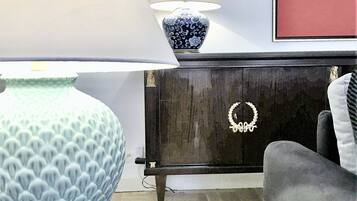 Ett vardagsrum med en stor blå vas, en bordslampa, ett skåp dekorerat med en krans och en inramad tavla på väggen.