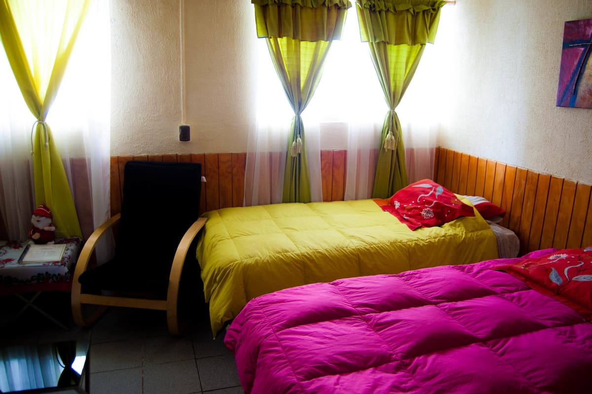 A room with two beds, a chair, and a small table with a Santa figurine.
