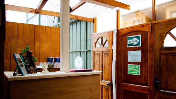 A wooden reception desk with a window, a green door with an 'ESCAPE' sign, and a 'SALIDA DE EMERGENCIA' sign. - Apart Hotel Bahia Caracoles (Antofagasta)