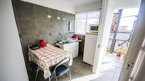 A compact kitchen with a tiled backsplash, a sink, a small refrigerator, and a dining area with a table and chairs. - Apart Hotel Bahia Caracoles (Antofagasta)