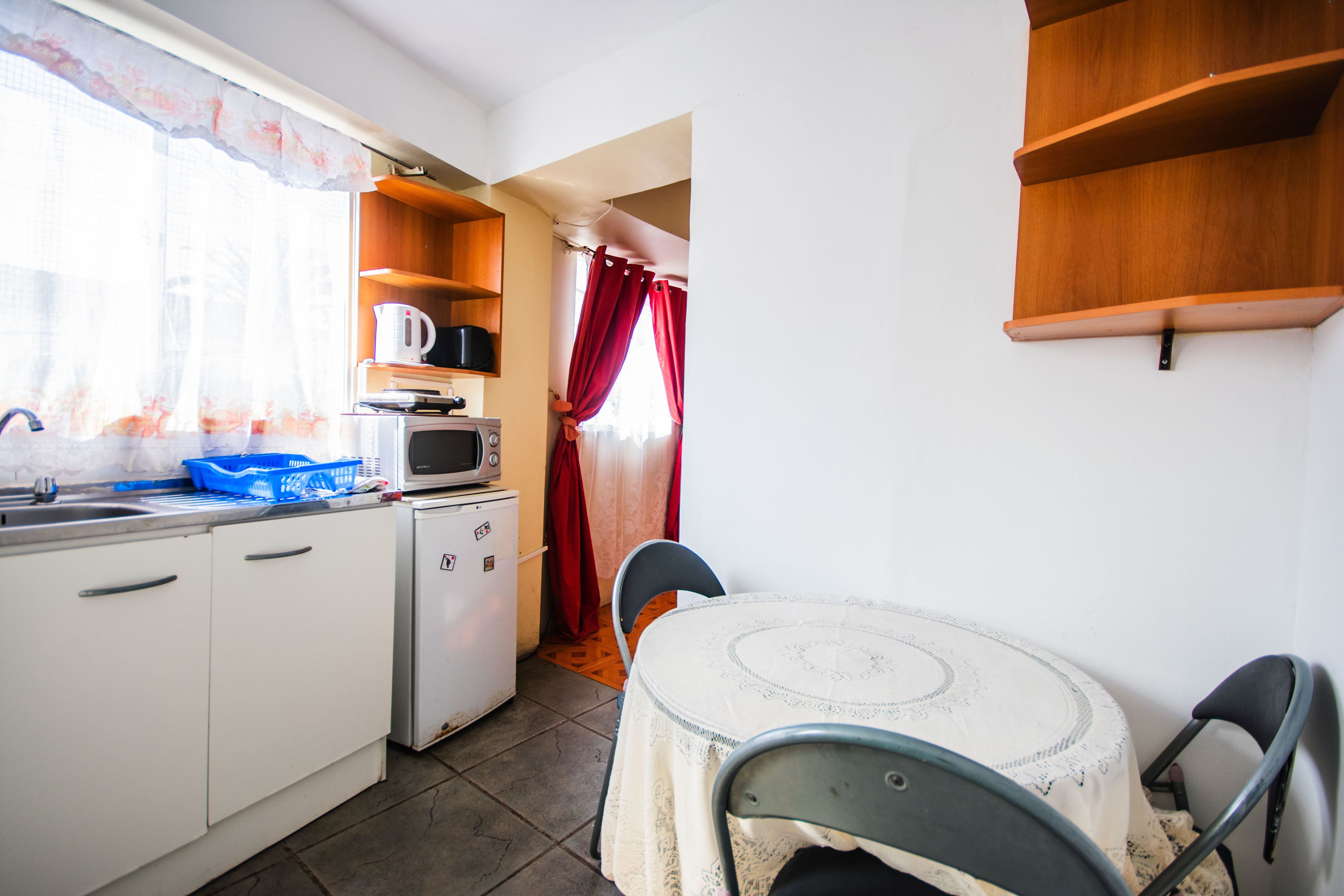 Una cocina compacta con armarios blancos, un microondas y un refrigerador pequeño. Hay una mesa con mantel blanco y dos sillas.