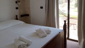 Quarto com uma cama grande, parede de pedra, uma mesa pequena e vista para o exterior.