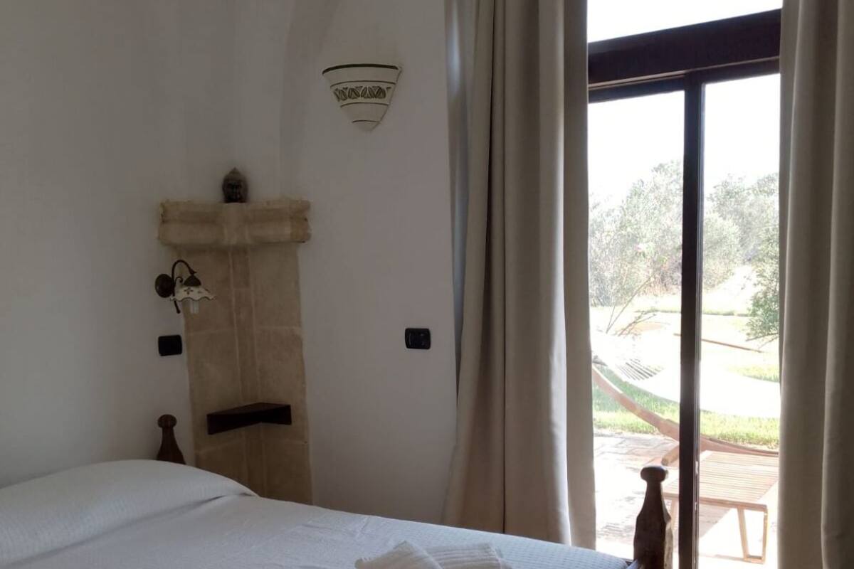 A bedroom with a large bed, a stone wall, a small table, and a view of the outdoors.