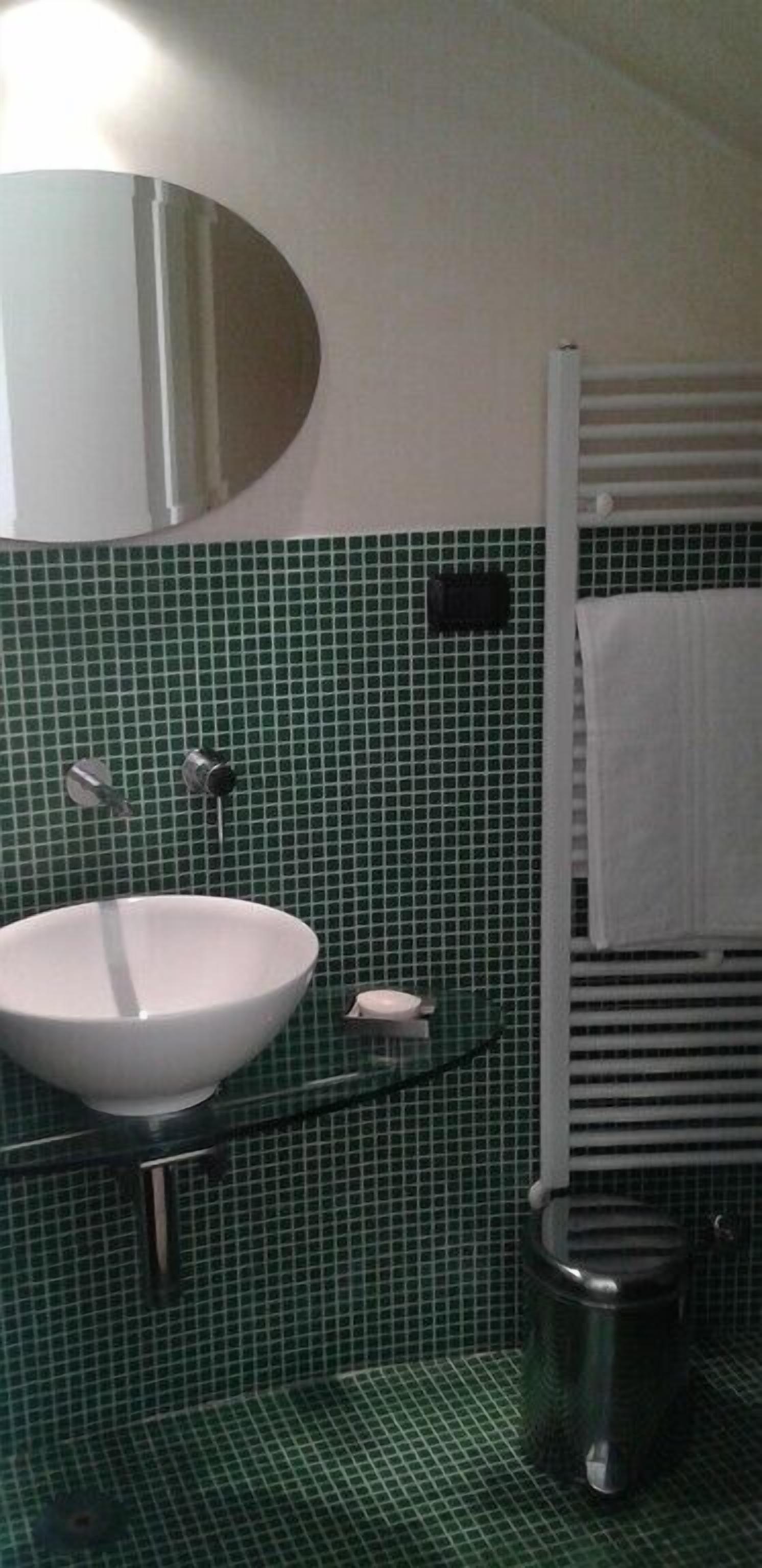 Une salle de bain avec un lavabo blanc, un miroir, un porte-serviettes et une poubelle.