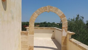 Um arco de pedra que dá acesso a um terraço no telhado, com vista para áreas verdes e edifícios ao longe.