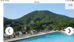 A swimming pool with lounge chairs and umbrellas, surrounded by a forested hillside.