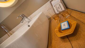 A bathroom with a bathtub, a mirror, and a wooden side table with a bottle of lotion and a glass.